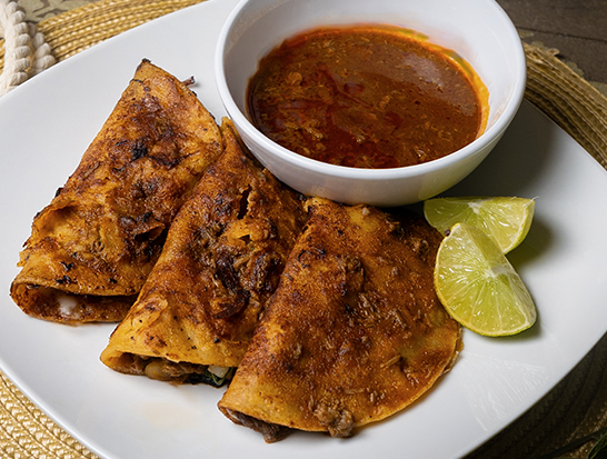 Quesabirrias - Crispy tortillas dipped in birria consommé, filled with tender slow-cooked birria meat